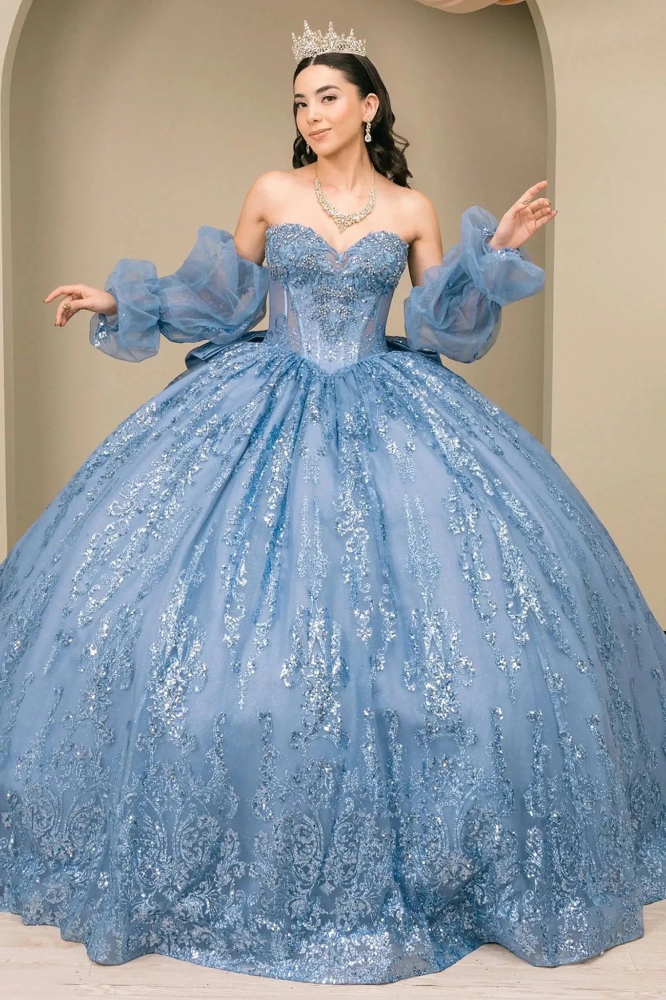 Woman wearing dusty blue off-shoulder sweetheart quinceañera dress with beaded sequin bodice and voluminous tulle skirt with dramatic sleeves
