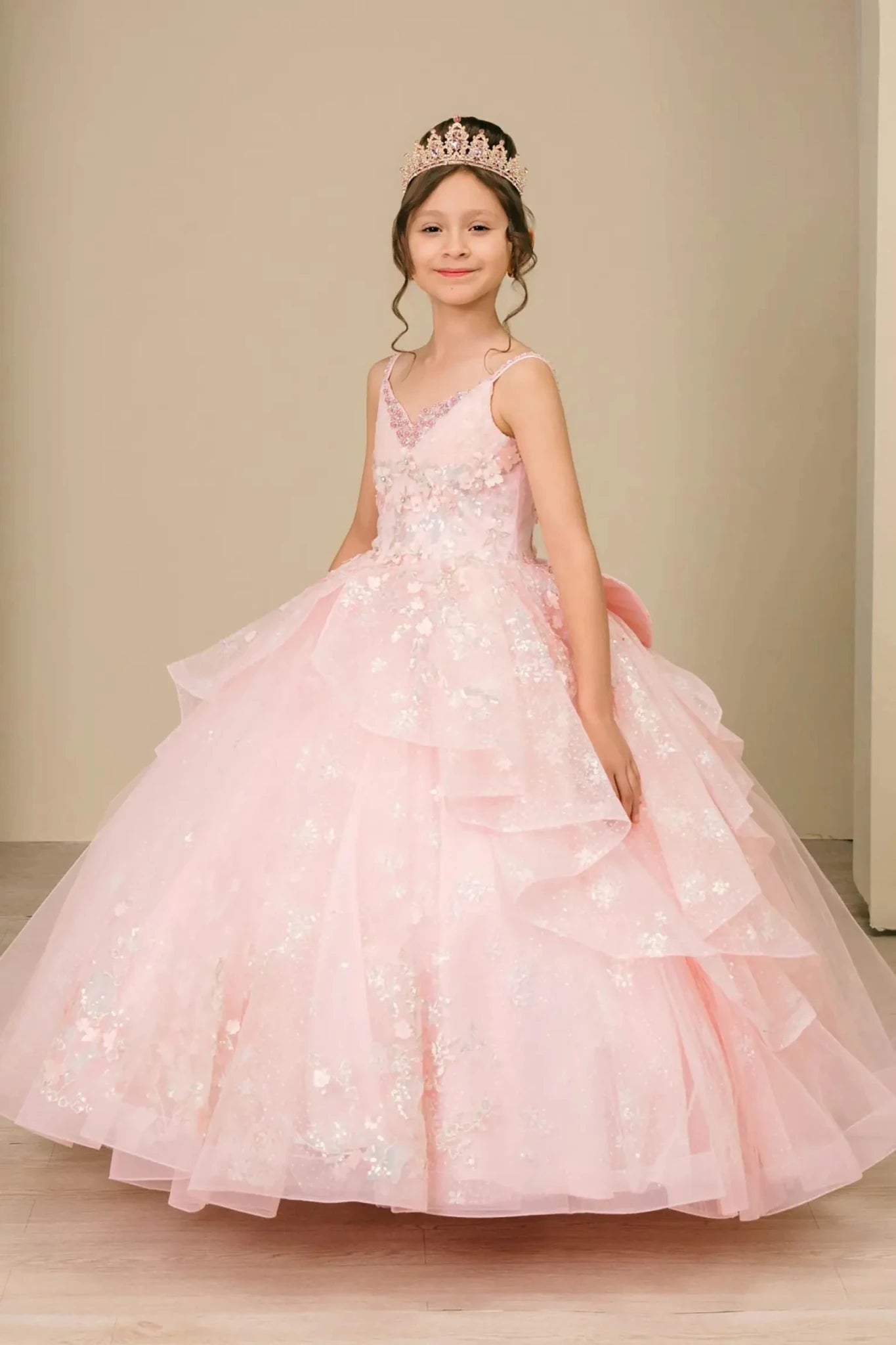 Young girl standing side-facing in mini quinceañera ball gown with V-neck corset bodice, sequin floral embroidery, and flowing layered skirt