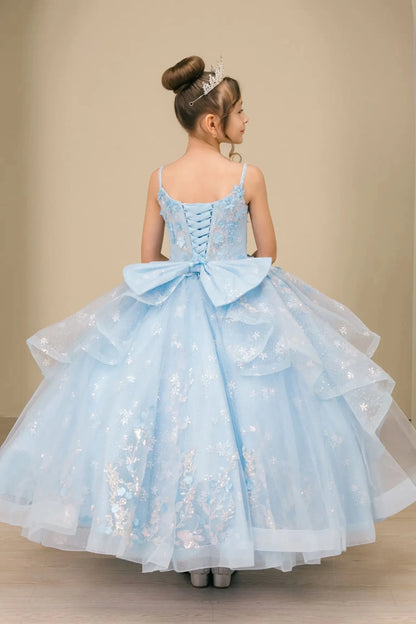 Young girl standing back-facing in mini quinceañera ball gown with lace-up corset bodice, oversized bow accent, and layered skirt