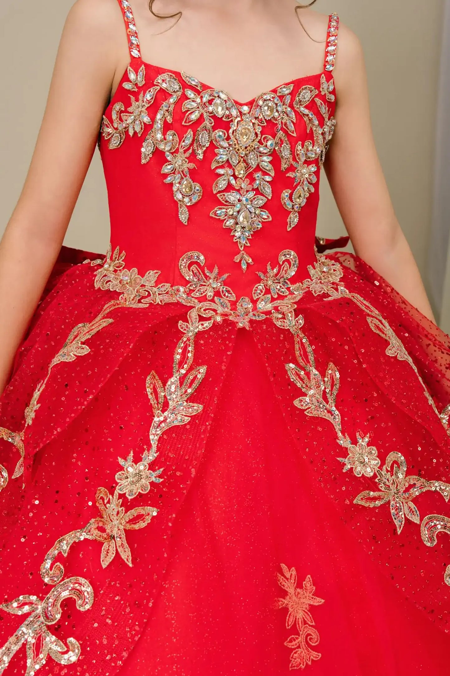 Bodice close-up of a red kids quinceañera dress showing gold embroidery, sequins, and floral applique details.