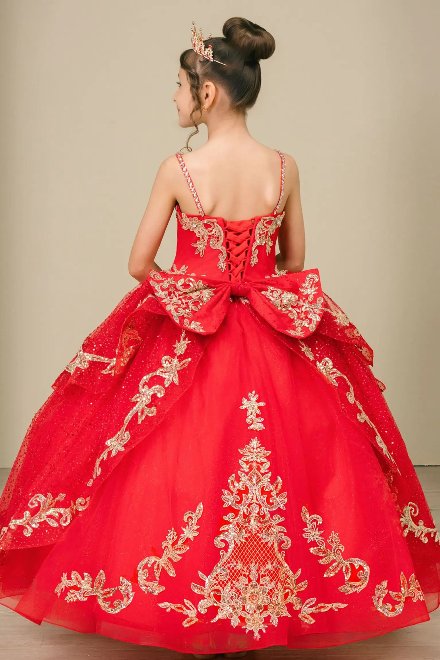Back view of a red kids quinceañera dress with voluminous layered skirt, lace-up corset closure, and gold embroidered accents.