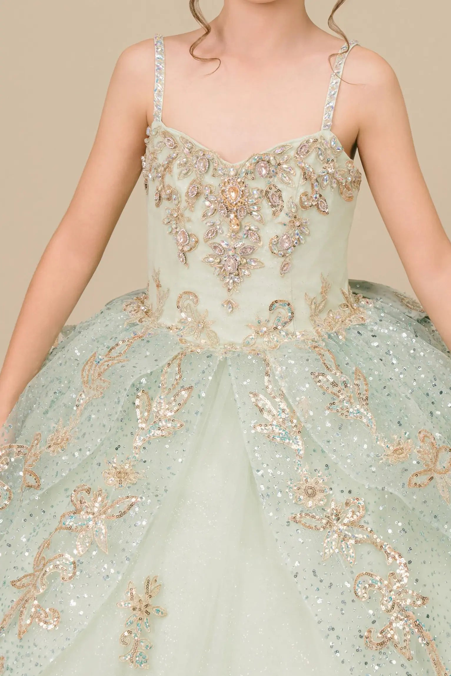 Bodice close-up of a sage kids quinceañera dress showing gold embroidery, sequins, and floral applique details.