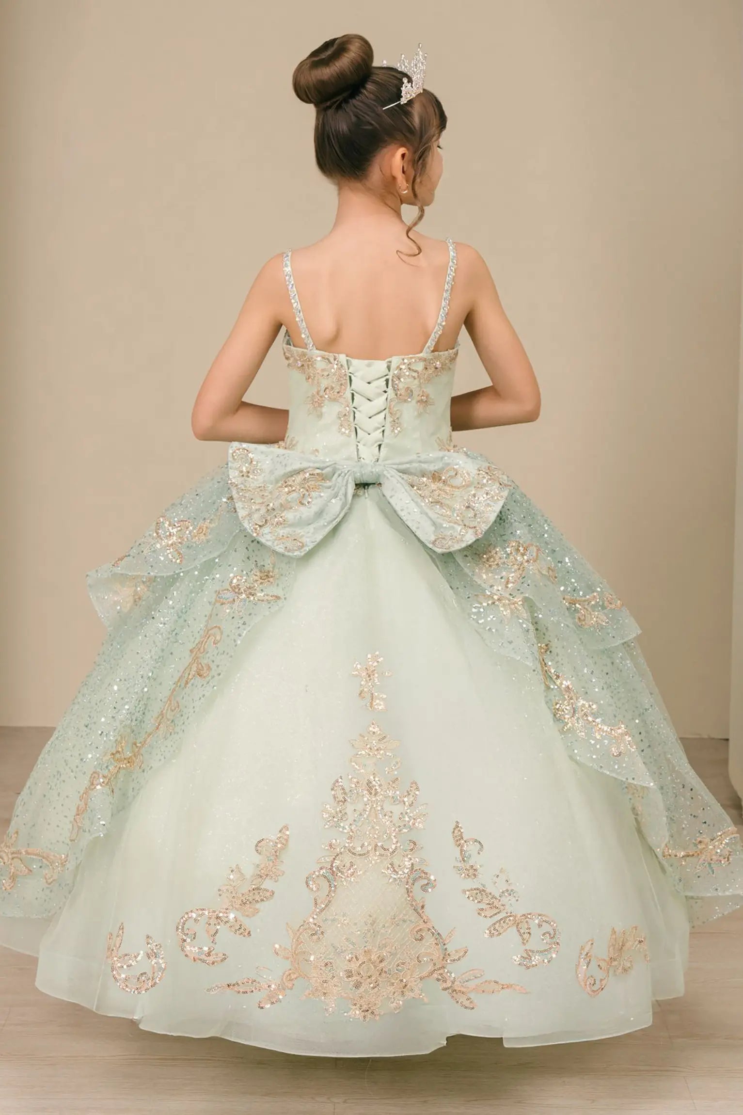 Back view of a sage kids quinceañera dress with voluminous layered skirt, lace-up corset closure, and gold embroidered accents.