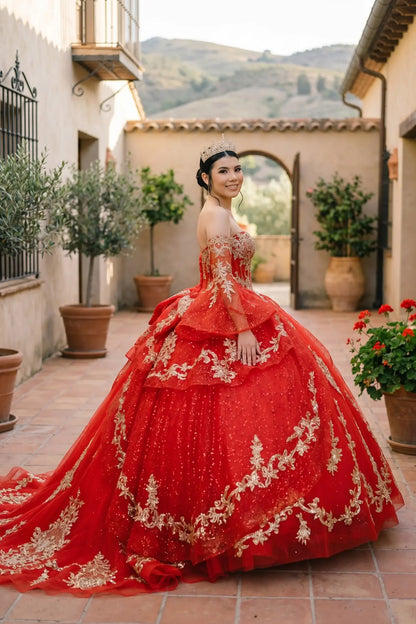 Side close-up view of a woman wearing red quinceañera dress highlighting ethereal sheer sleeves, embroidered bodice, and layered glitter tulle skirt.