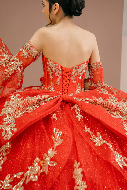 Bodice back close-up of a woman wearing red quinceañera dress with gold embroidery, sequins, and lace-up corset design framed by flowing sleeves.