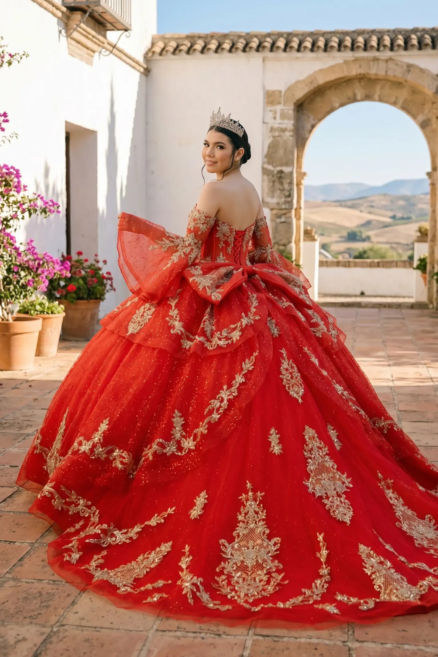 Back view of a woman wearing red quinceañera dress with voluminous glitter tulle skirt, lace-up corset closure, and gold embroidered embellishments.