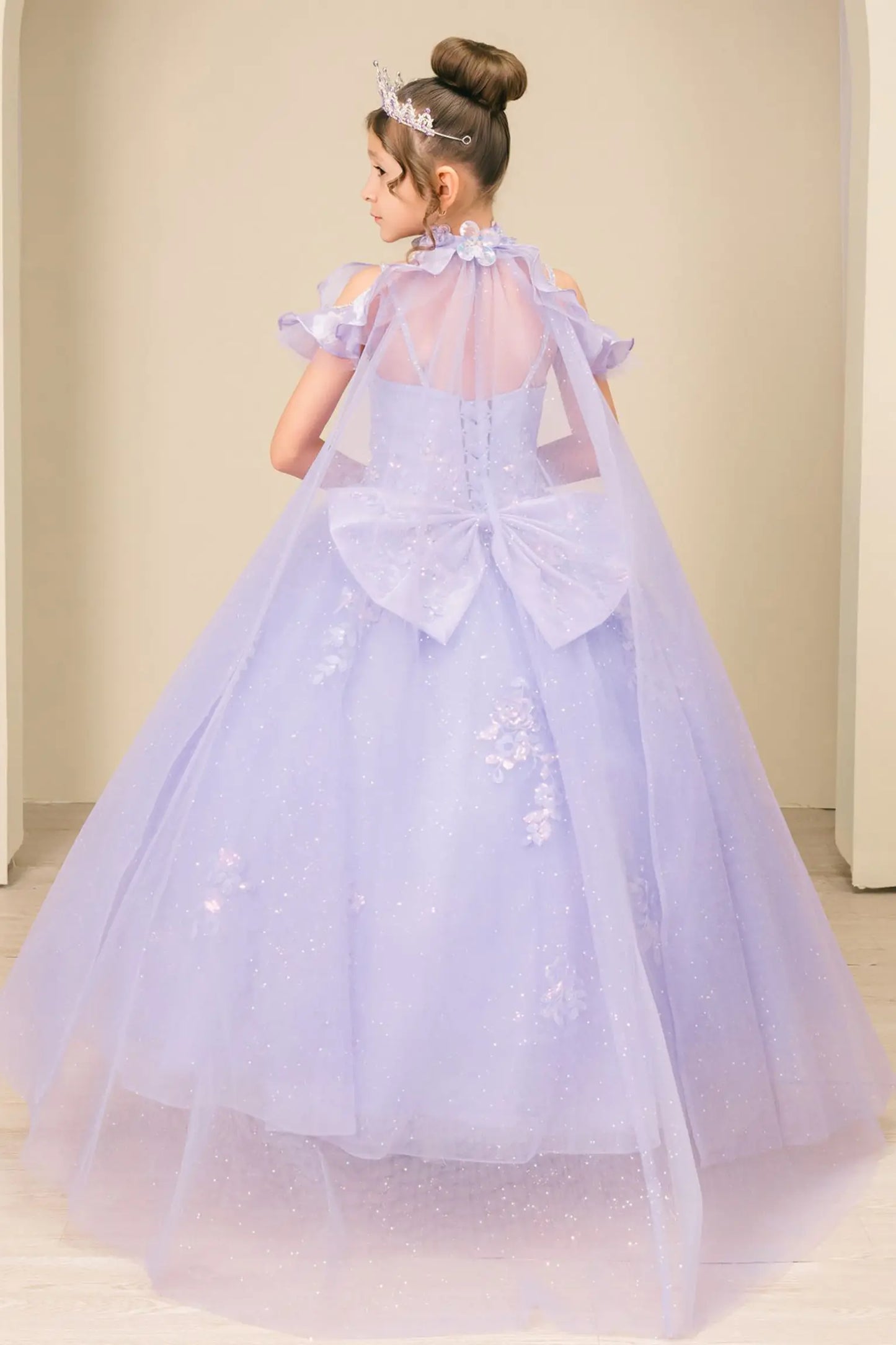 Back view of a kid wearing lilac mini quinceañera dress with voluminous tulle skirt, lace-up corset closure, and floral appliques trailing across the bodice.
