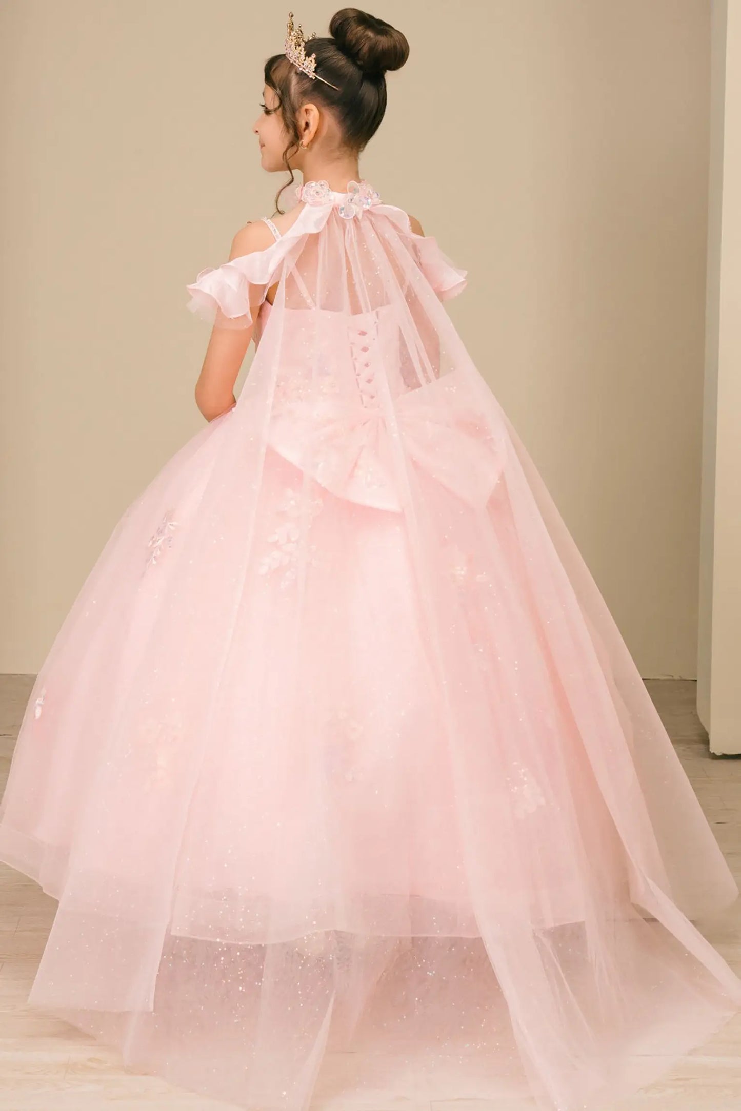 Back view of a woman wearing pink mini quinceañera dress with voluminous tulle skirt, lace-up corset closure, and floral appliques trailing across the bodice.