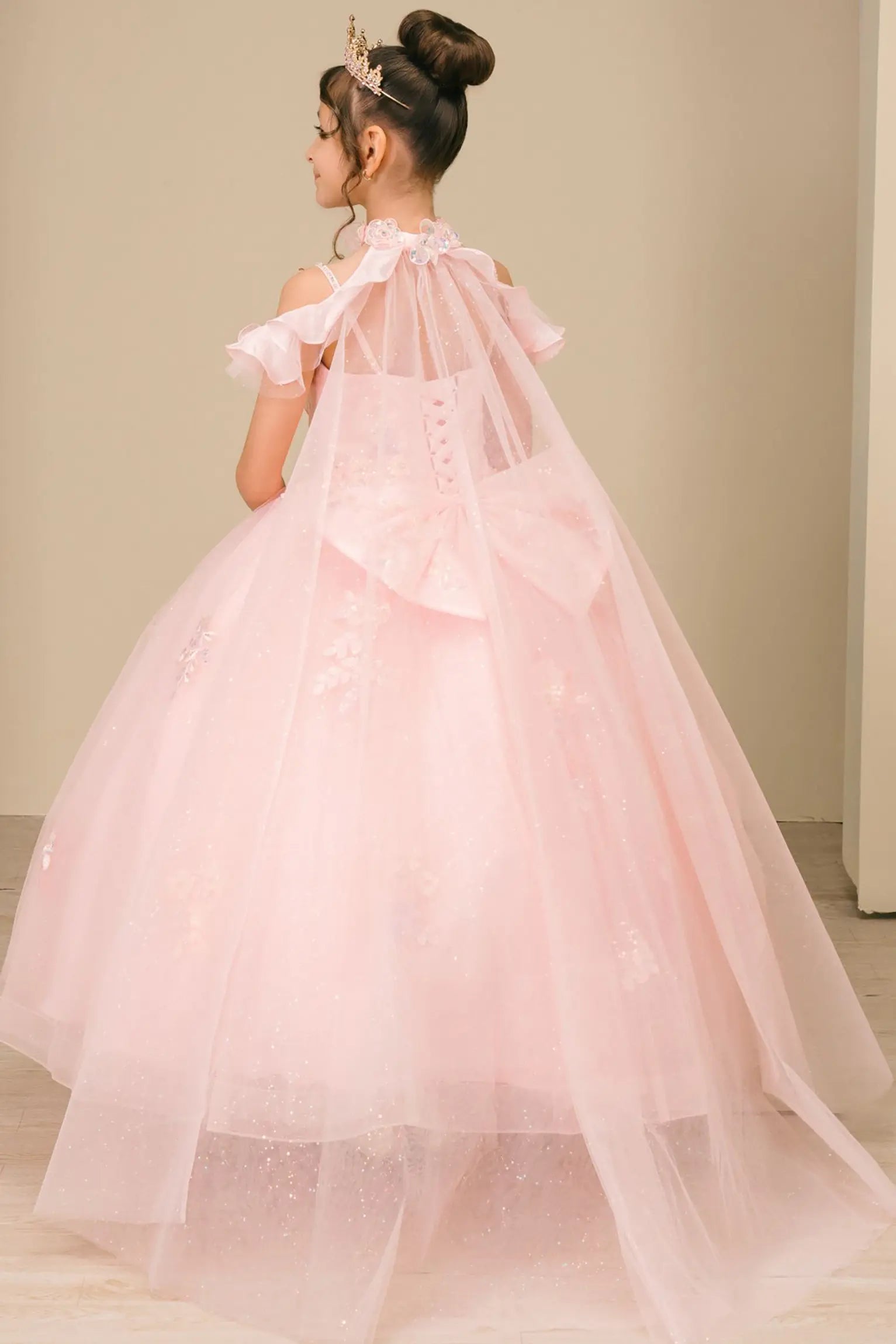 Back view of a woman wearing pink mini quinceañera dress with voluminous tulle skirt, lace-up corset closure, and floral appliques trailing across the bodice.