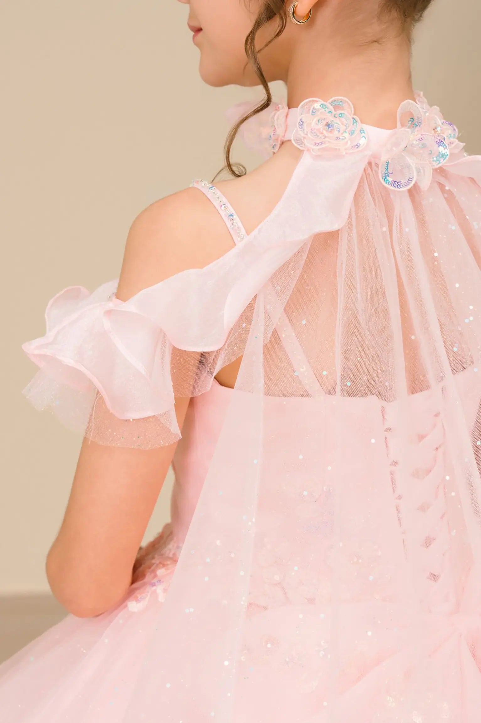 Close Up back view of a woman wearing pink mini quinceañera dress with voluminous tulle skirt, lace-up corset closure, and floral appliques trailing across the bodice.