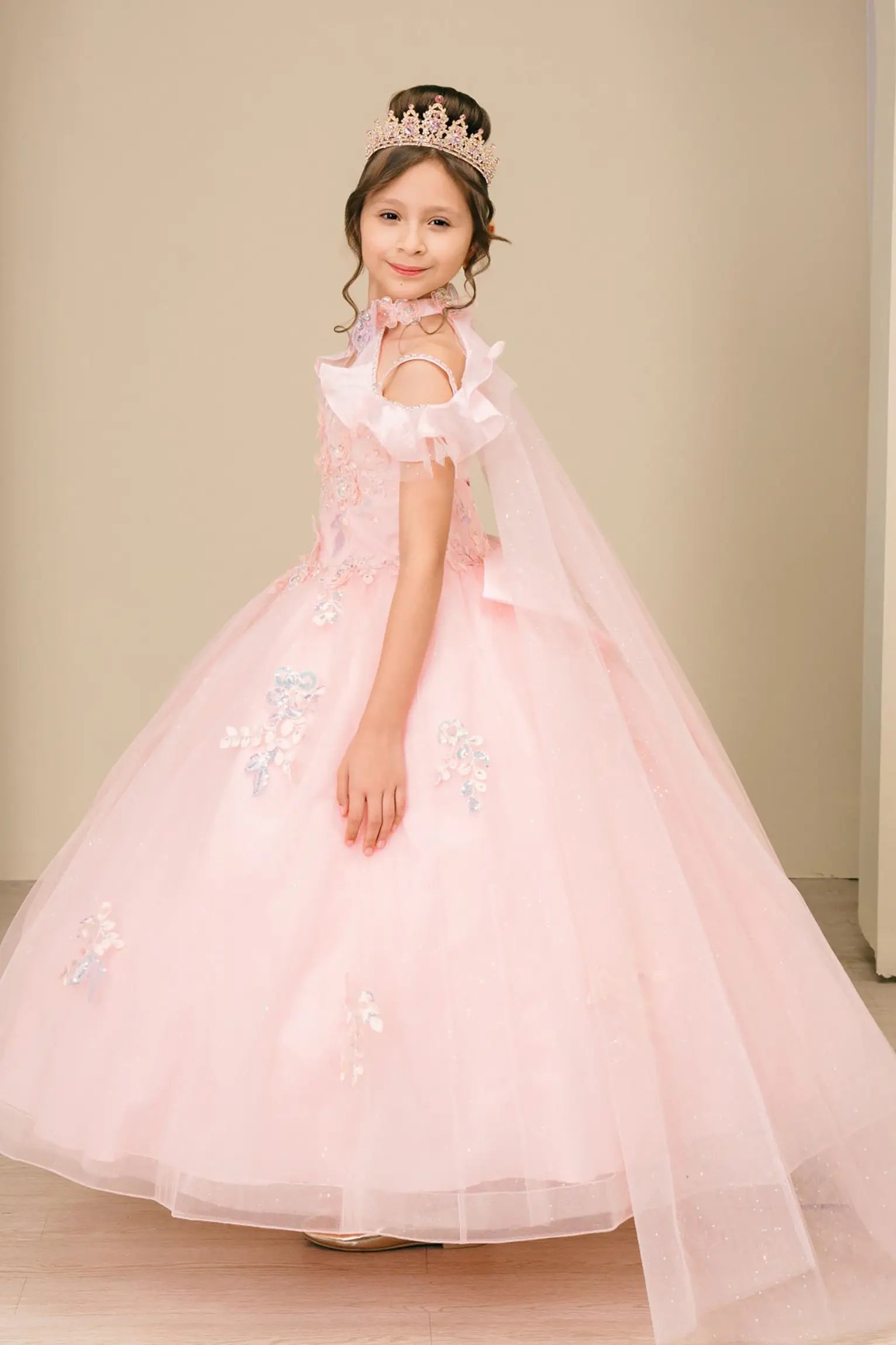 Side close-up view of a woman wearing pink mini quinceañera dress highlighting layered tulle skirt, ruffled off-shoulder sleeves, and sparkling embellished bodice.