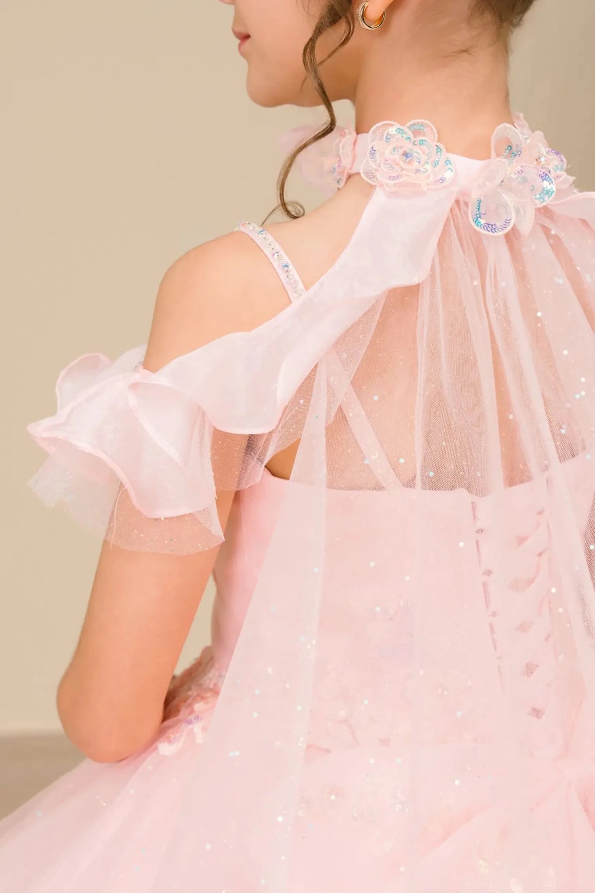 Rear view reveals a pink mini quinceañera mini quince dress with voluminous tulle skirt, lace-up corset closure.
