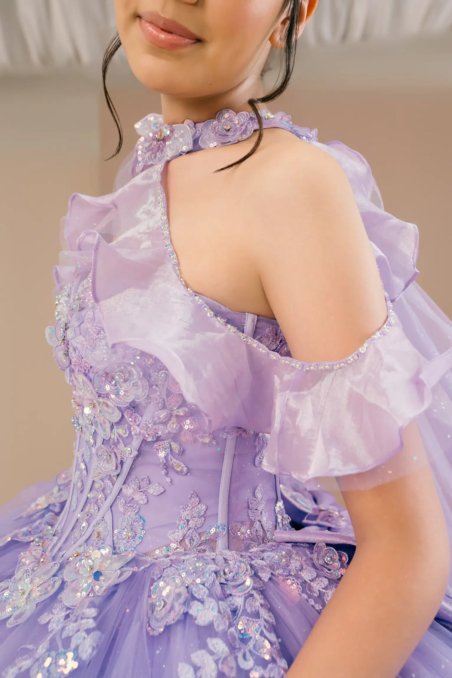 Side close-up view of a woman wearing lilac quinceañera dress highlighting layered glitter tulle, off-shoulder ruffles, and embellished bodice.