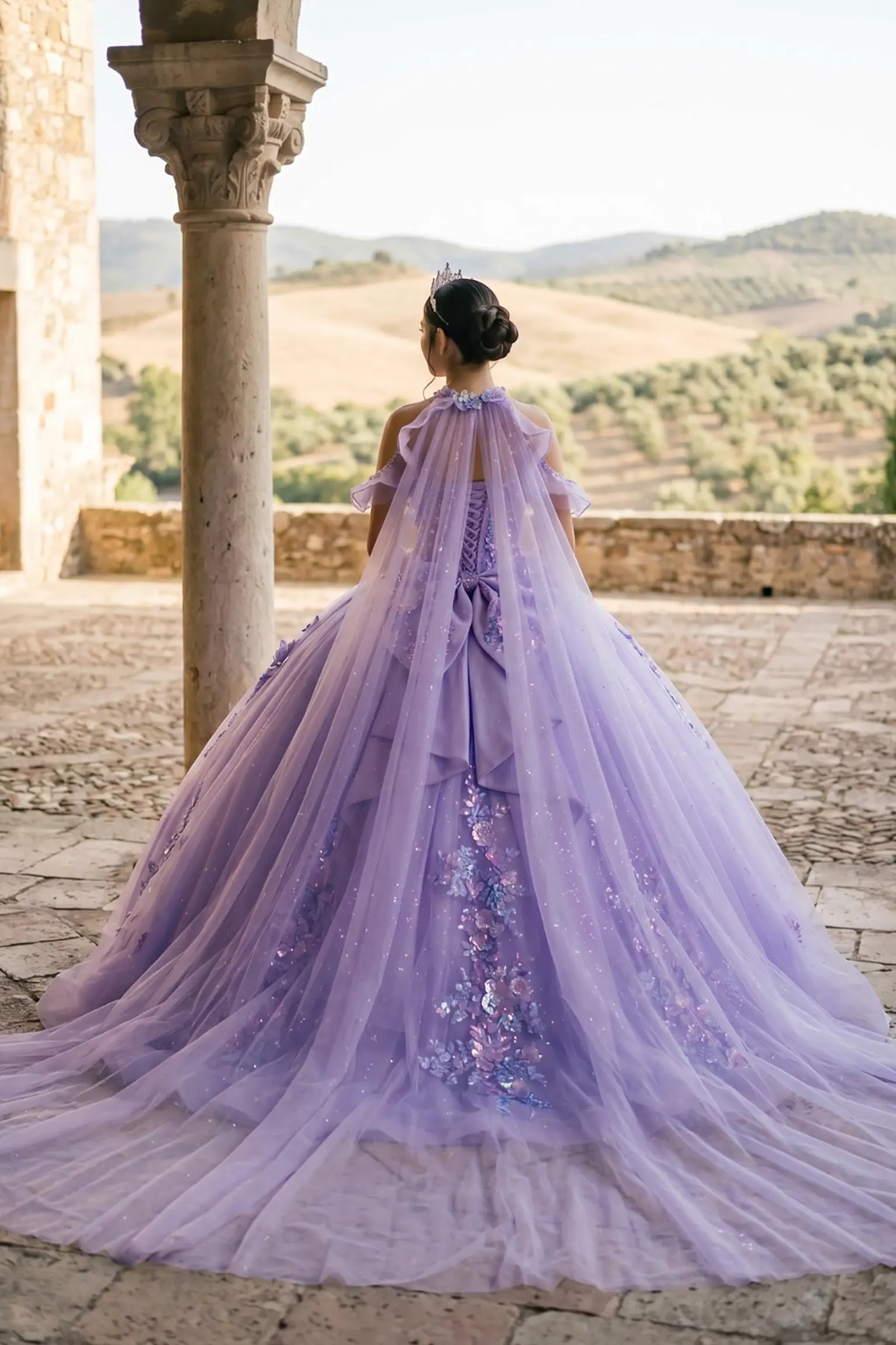 Back view of a woman wearing lilac quinceañera dress with voluminous tulle skirt, lace-up corset closure, and floral appliques trailing across the bodice.
