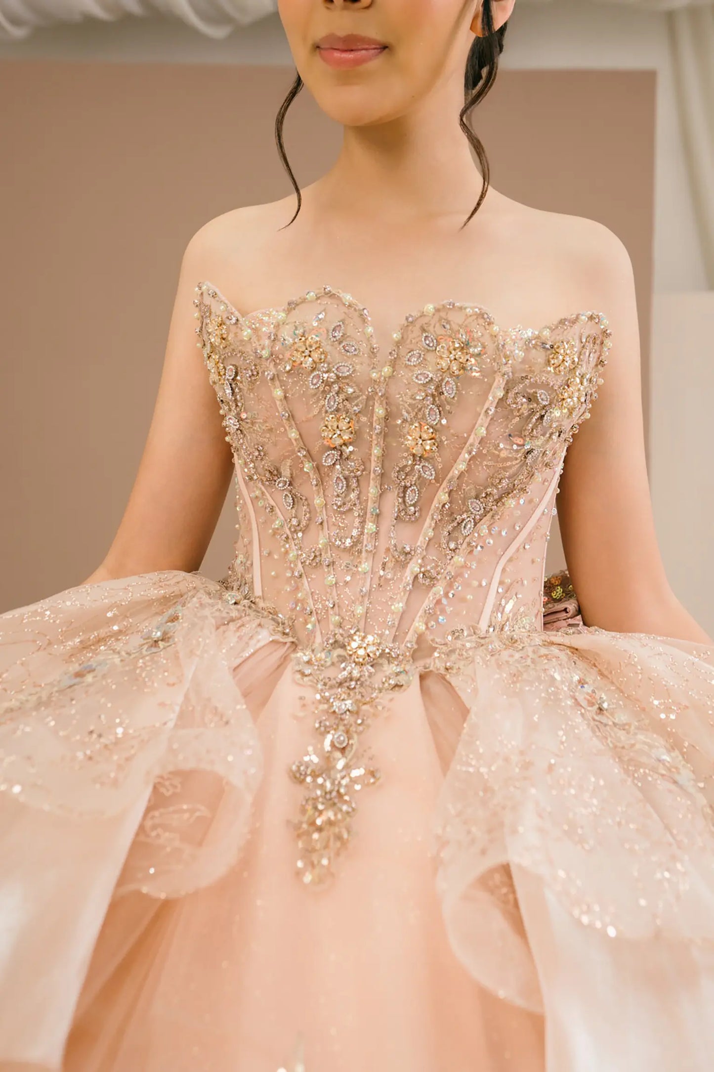 Bodice close-up of a woman wearing rose gold quinceañera dress showing intricate beadwork, floral applique details, and sparkling sequins.