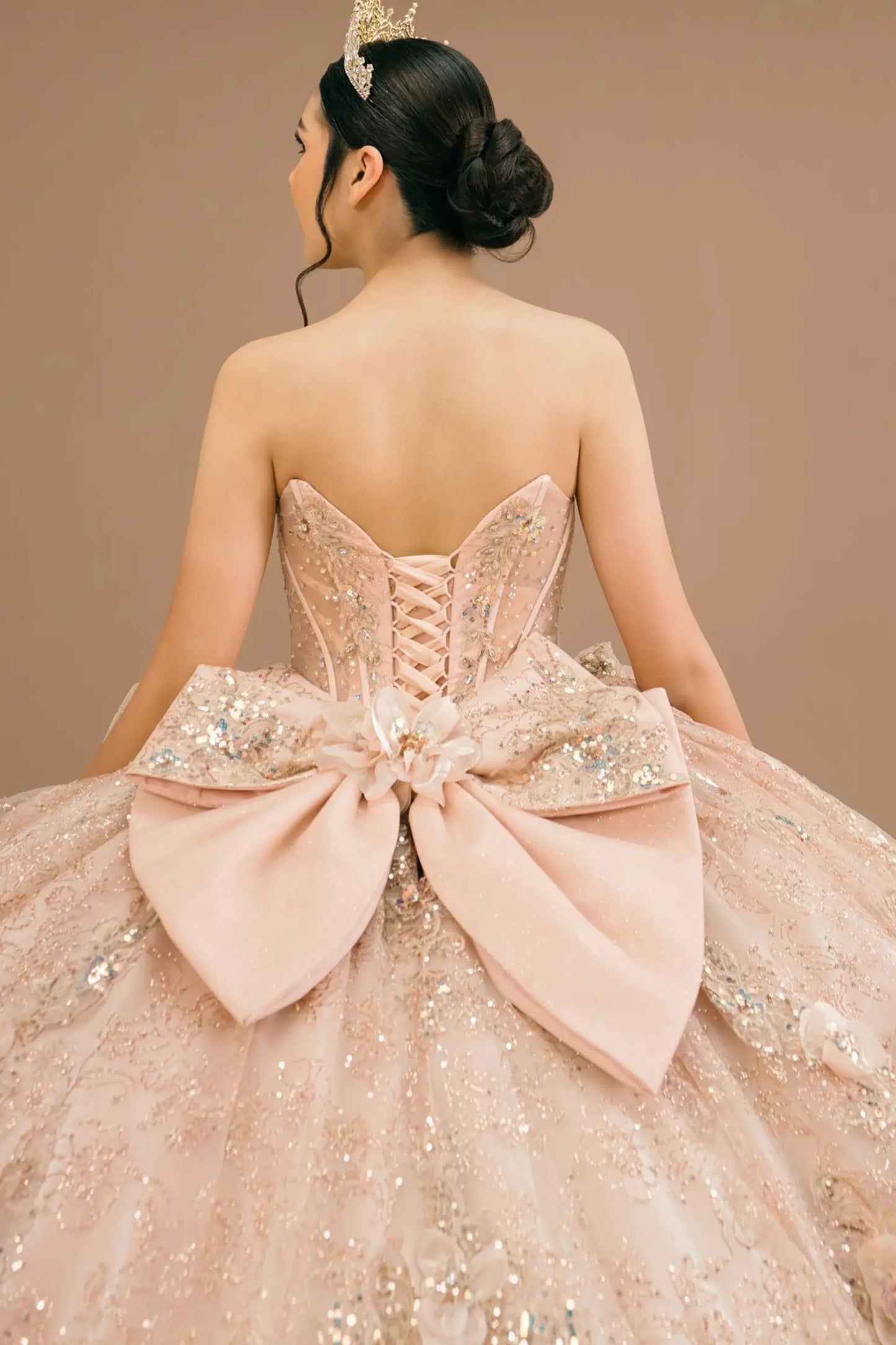 Bodice back close-up of a woman wearing rose gold quinceañera dress with beadwork detail, sequins, and lace-up corset design.