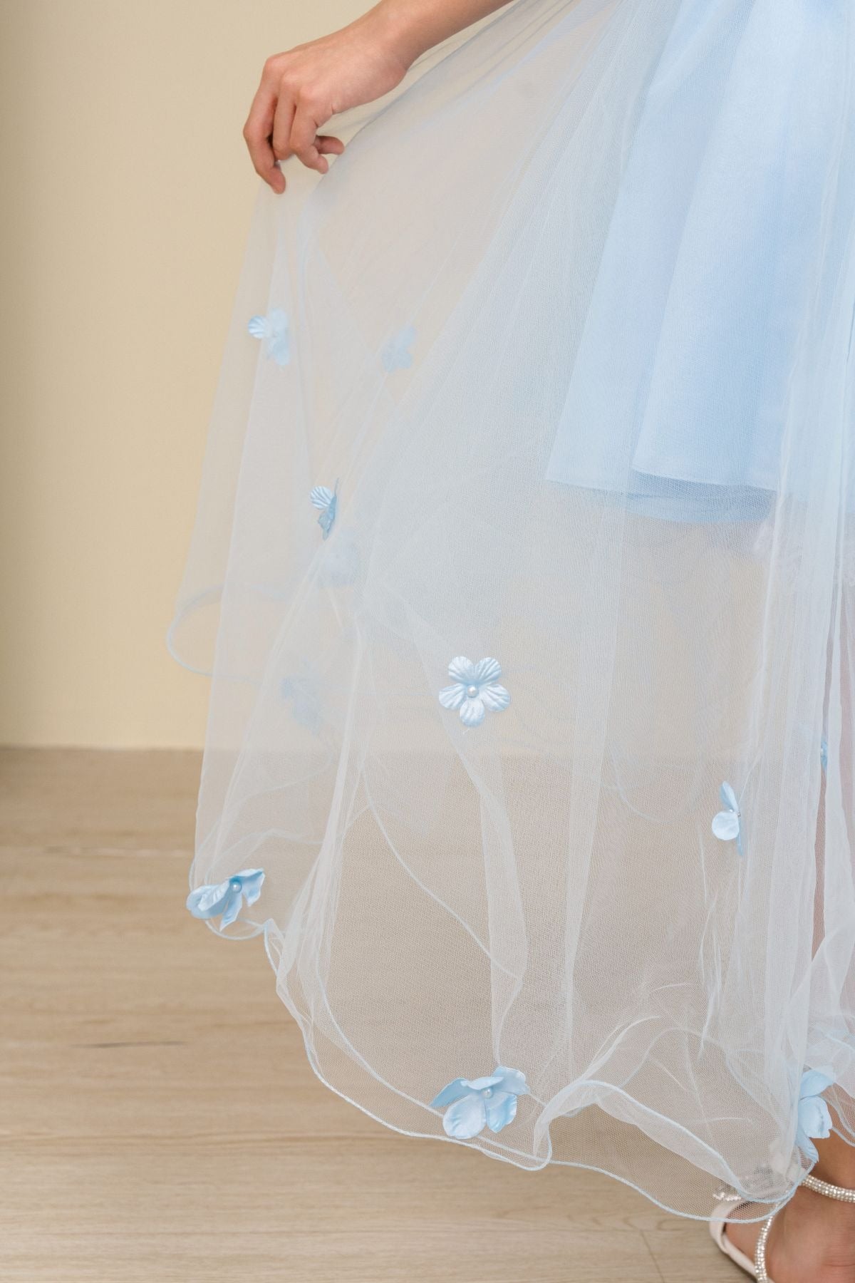 Close-up of sky blue high-low tulle flower girl dress fabric with 3D floral appliqué embroidery and layered tulle texture.