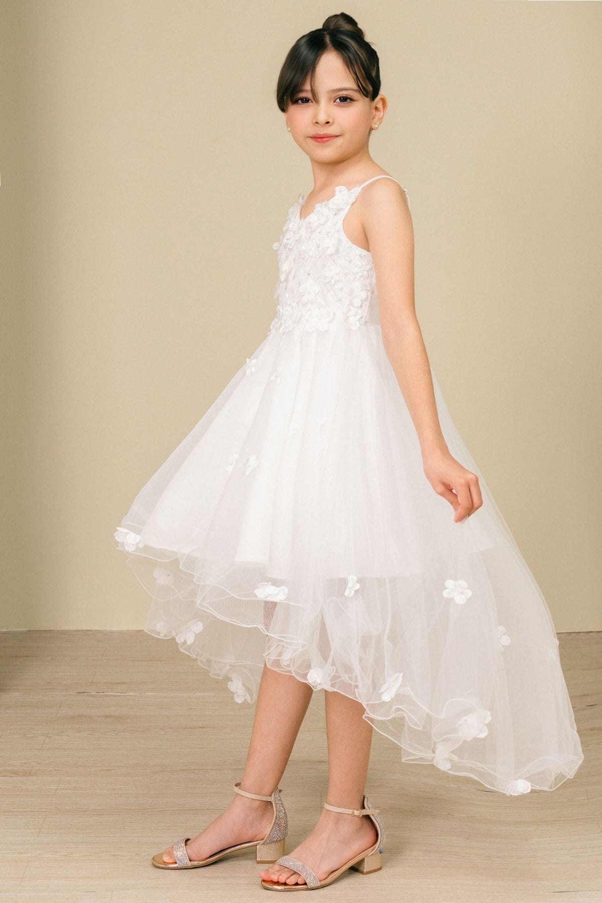 Side view of white high-low tulle flower girl dress with 3D floral appliqué detailing and flowing layered high-low skirt.