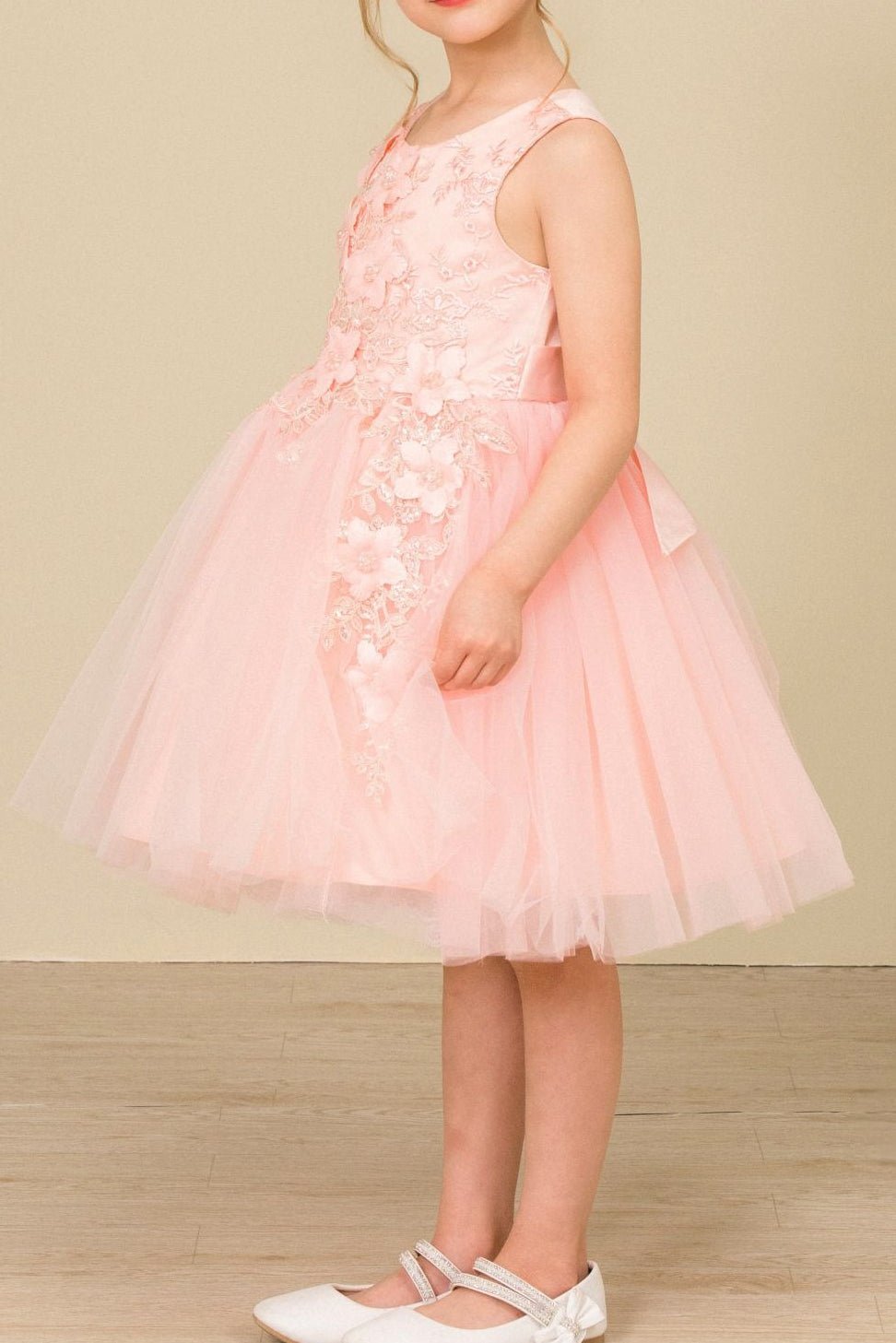 Side view of blush sleeveless flower girl dress with 3D floral appliqué detailing and voluminous wired tulle skirt.