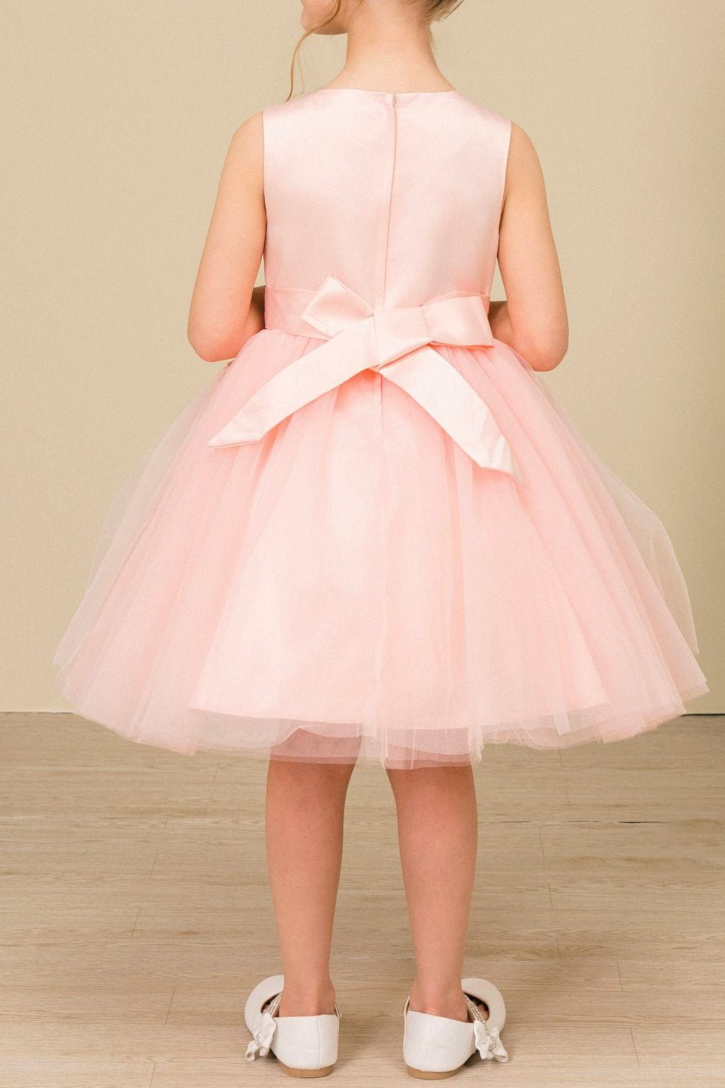 Back view of blush sleeveless flower girl dress with lace-up bodice, 3D floral appliqué accents, and wired tulle skirt.