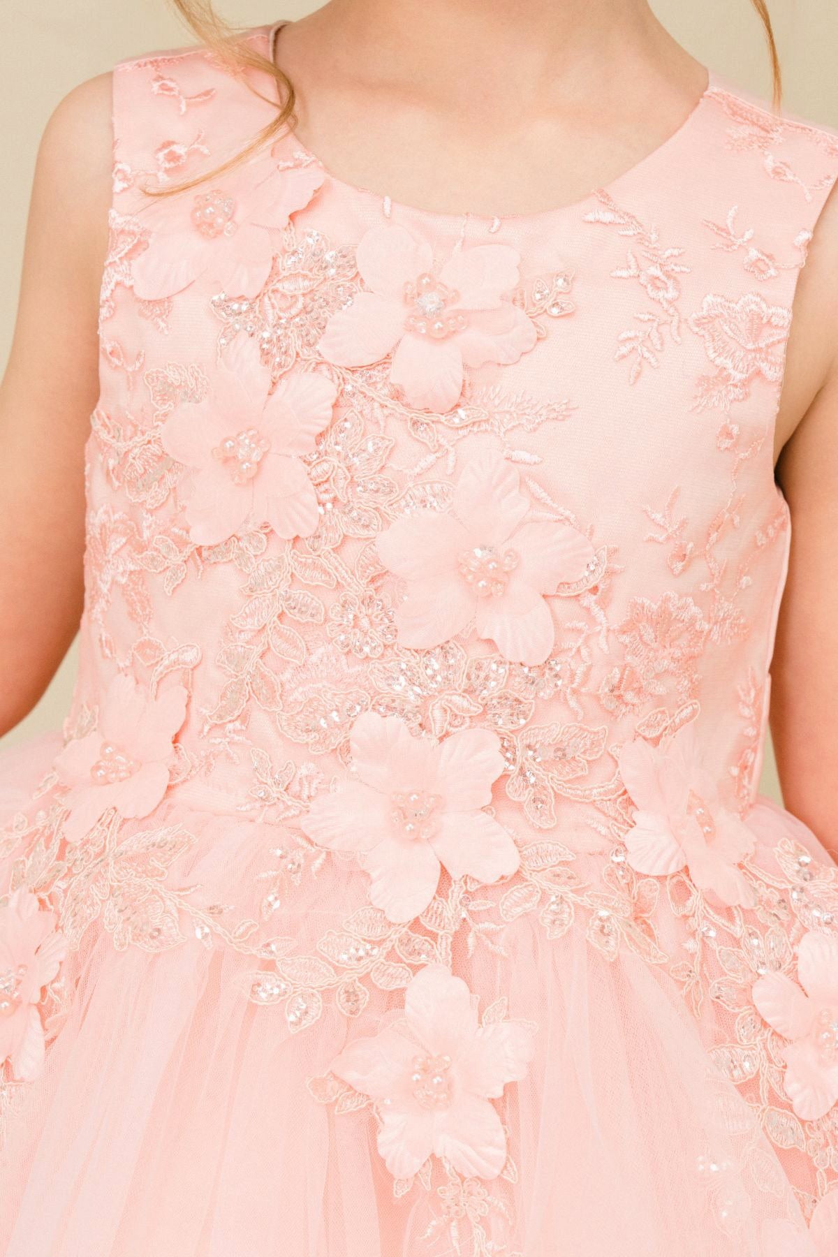 Close-up front-facing view of blush sleeveless flower girl dress with 3D floral appliqué bodice and elegant neckline.