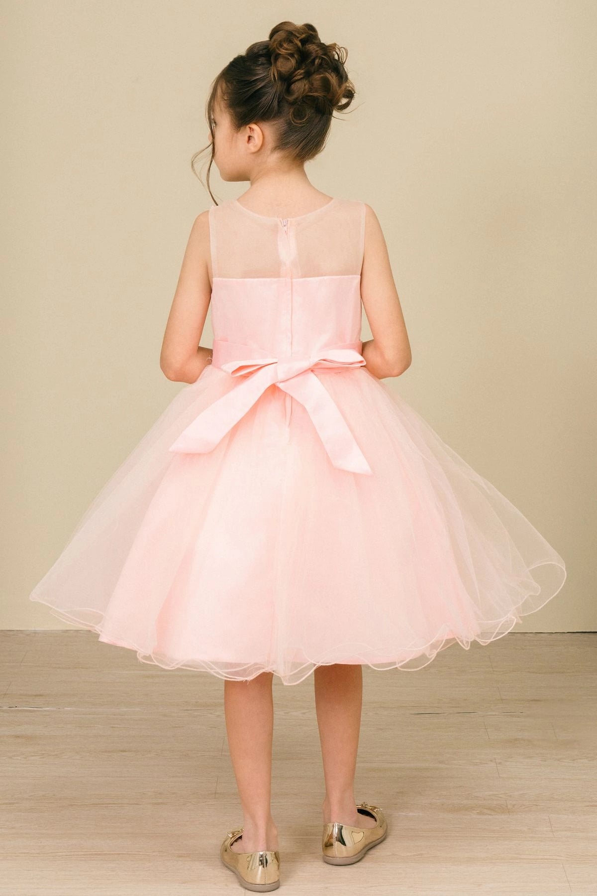 A Peach flower girl dress showing satin bow below the sheer back yoke.