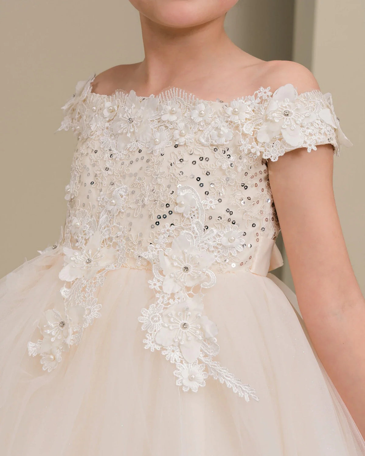 Close-up of a detailed off-shoulder champagne flower girl dress with floral and sequin embellishments.