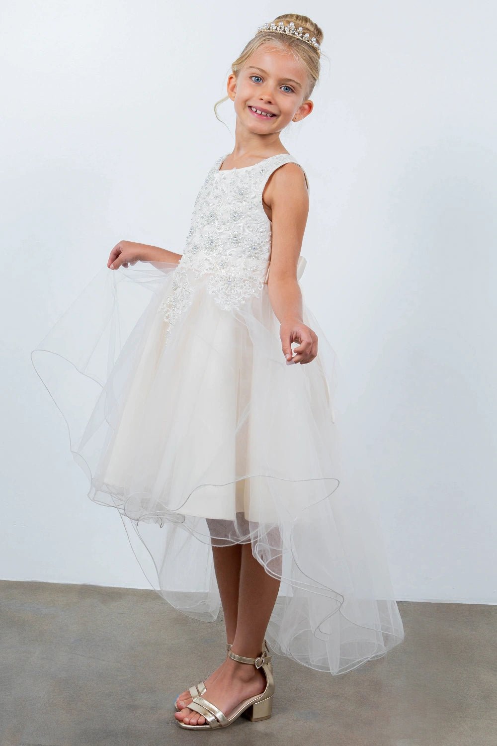 Shown in a angled view, the Champagne flower girl dress has sleeveless embellished bodice and layered high-low tulle skirt.