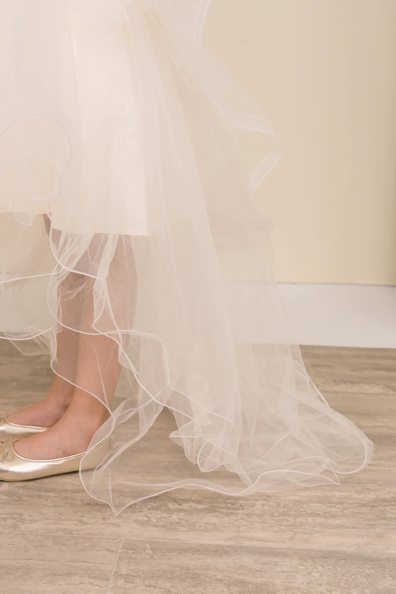 Close-up of champagne sleeveless high-low tulle flower girl dress fabric with lace embroidery, pearl trim accents, rhinestone sparkle, and shimmering tulle layers.