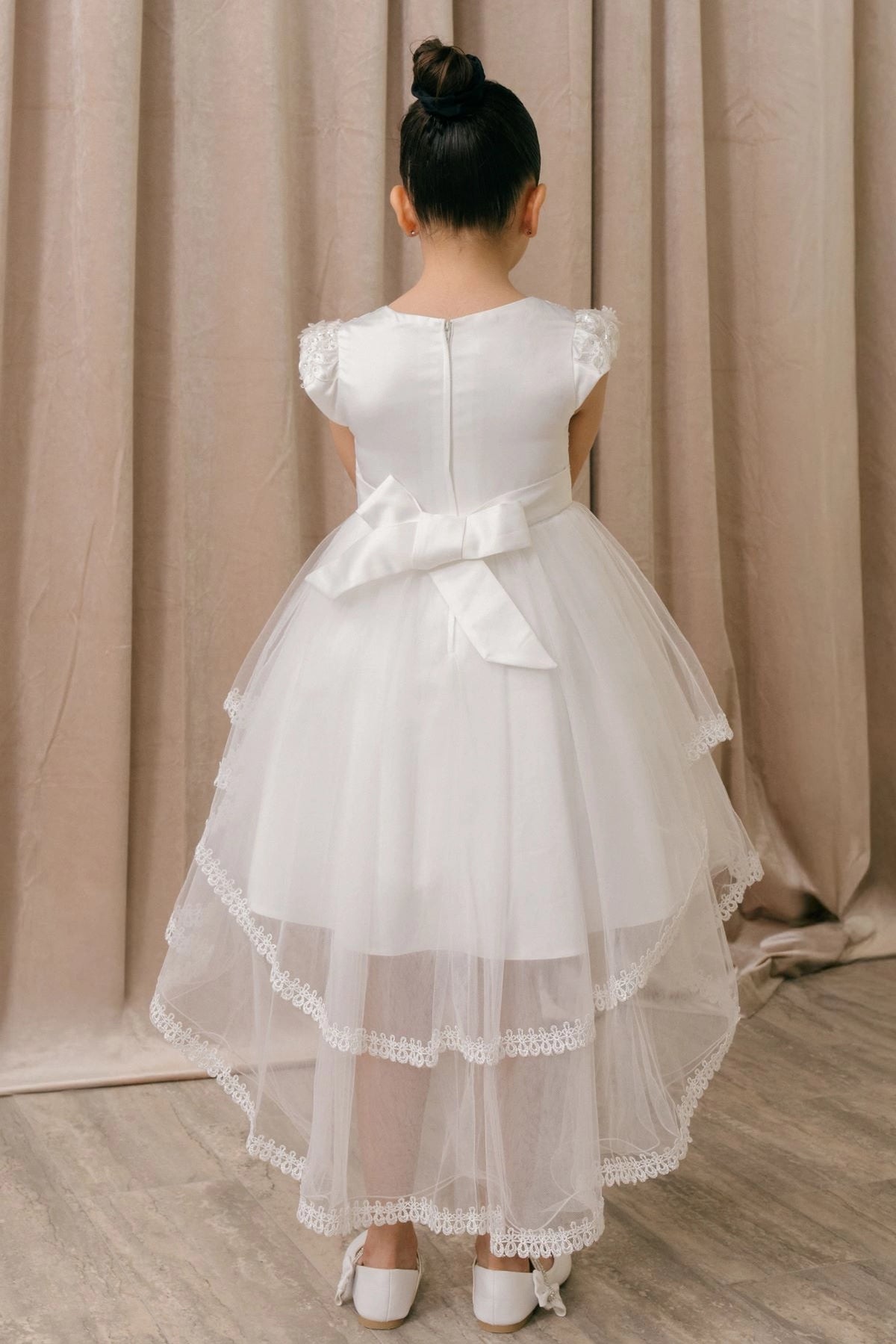 A White flower girl dress showing satin back bow above lace-trimmed tulle.