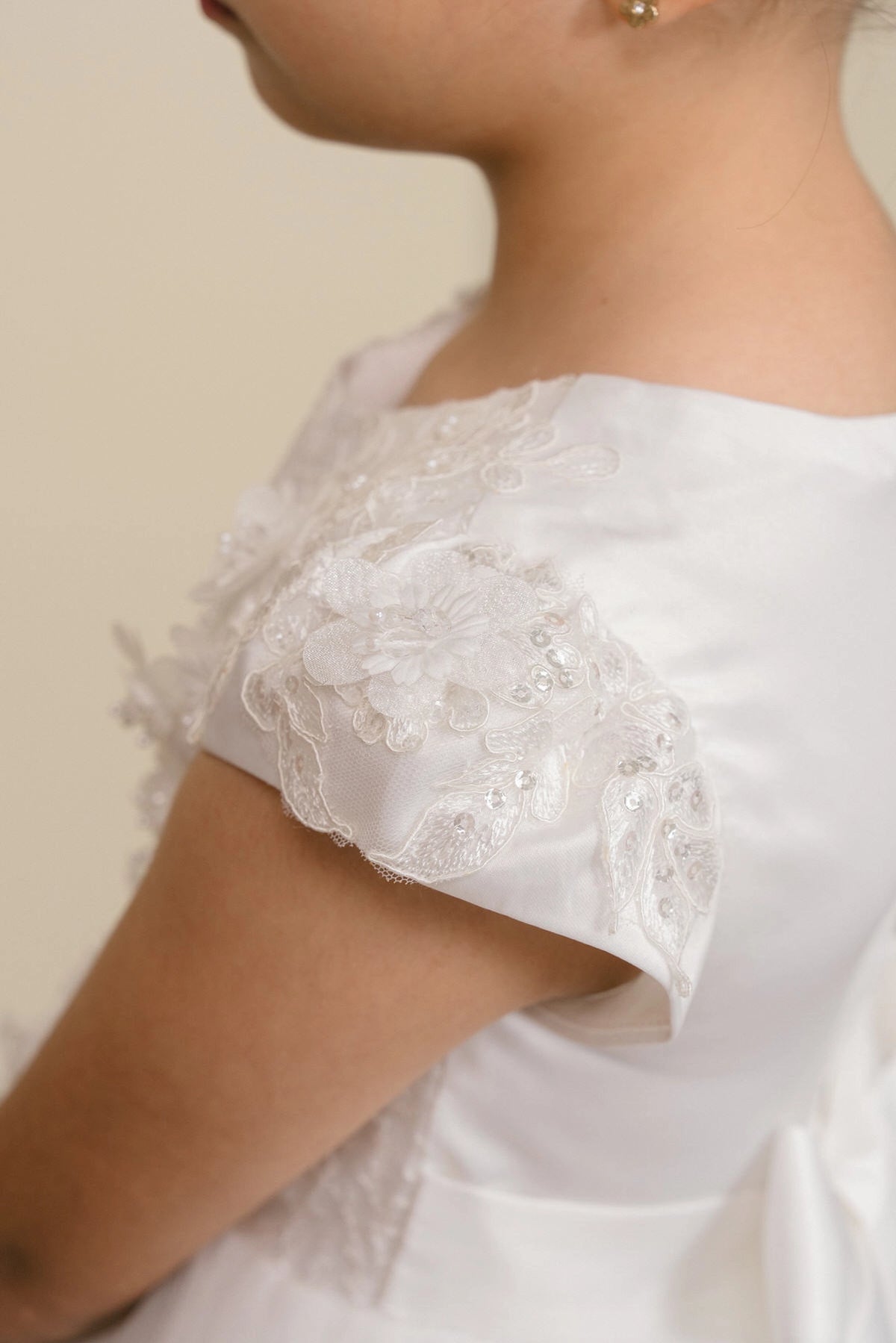 Details of the White flower girl dress include floral lace cap sleeve above the satin back.