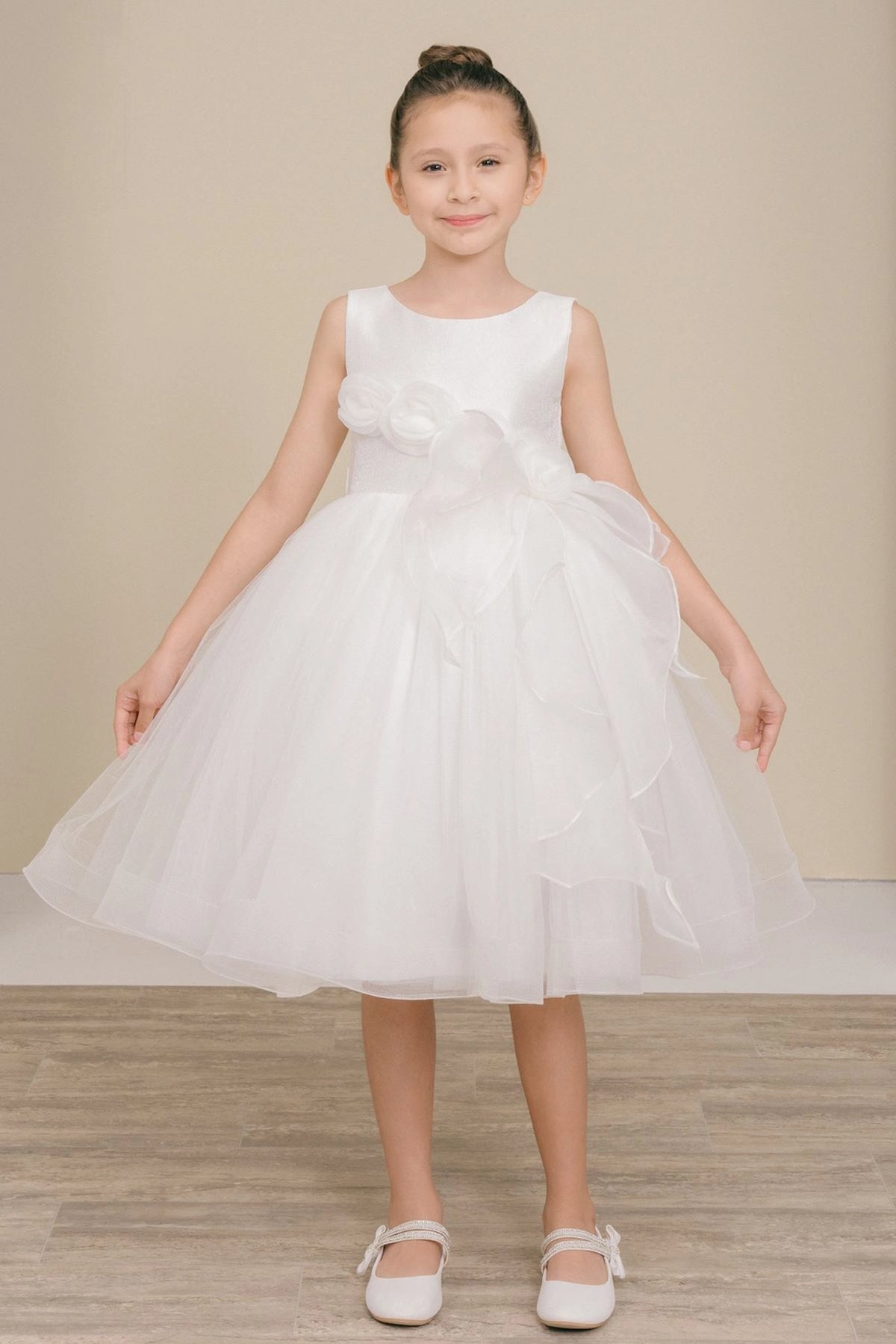 White flower girl dress features floral waist above cascading skirt ruffles.