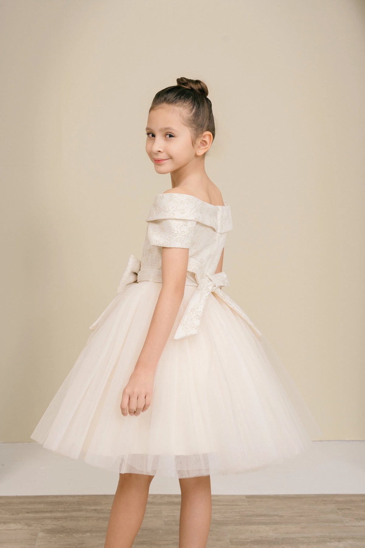 Showcasing with a folded off-shoulder neckline, this Champagne kids party dress displays elegant detail.