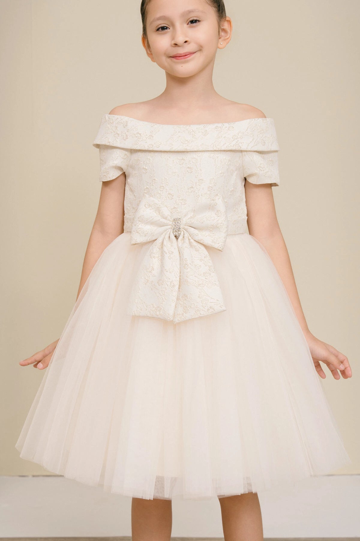 Accented a folded off-shoulder neckline adds character to this Champagne kids party dress.