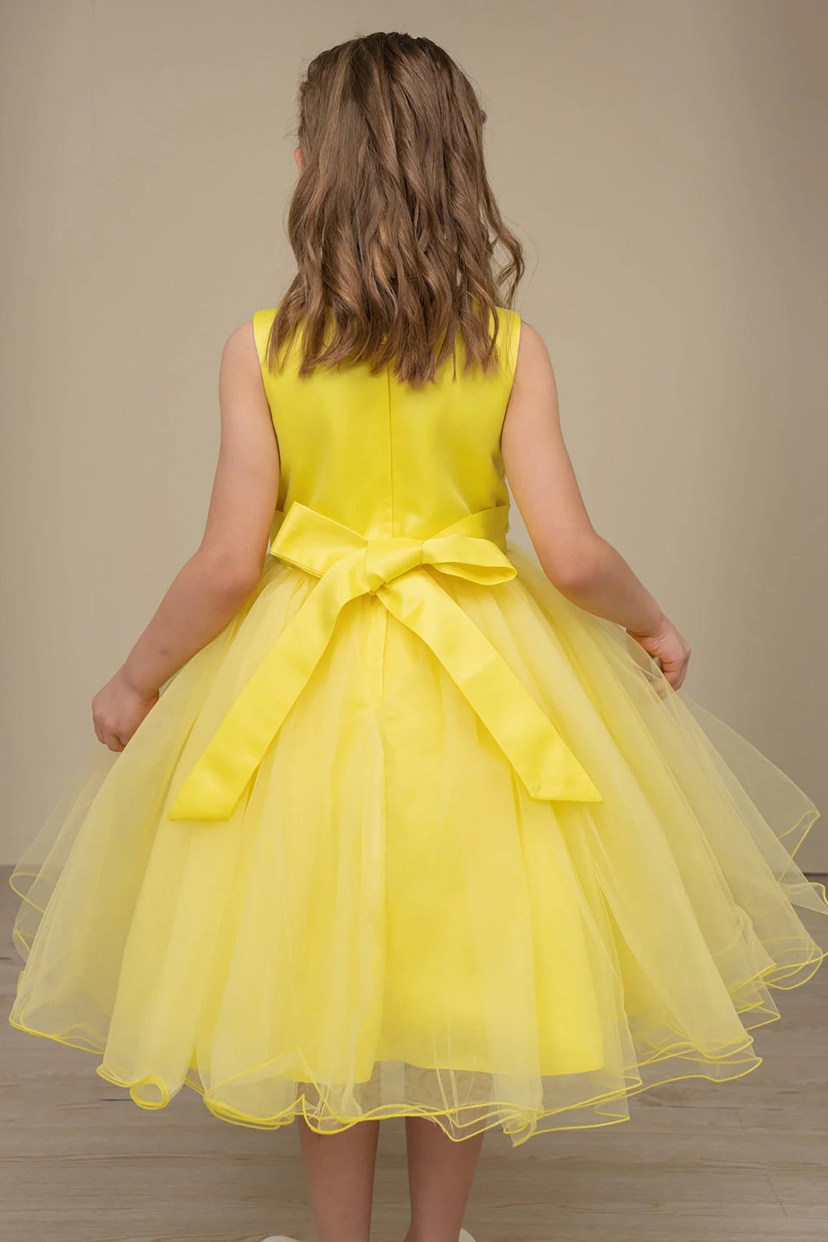 A yellow flower girl dress with a bow at the back.