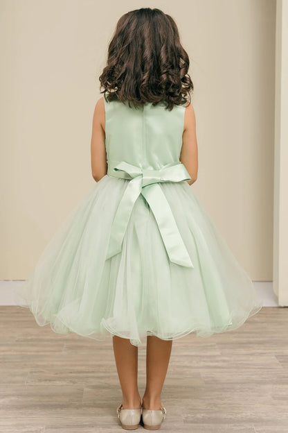 Child wearing a sage dress with a bow on a neutral background