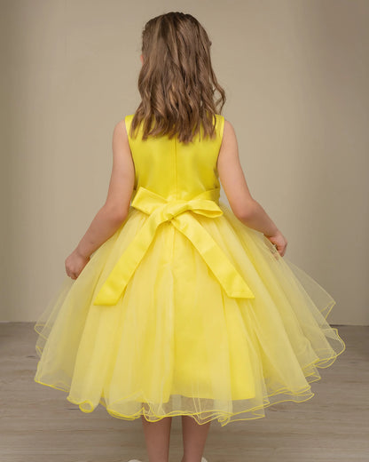 Young girl wearing a yellow dress with a bow at the back against a plain background