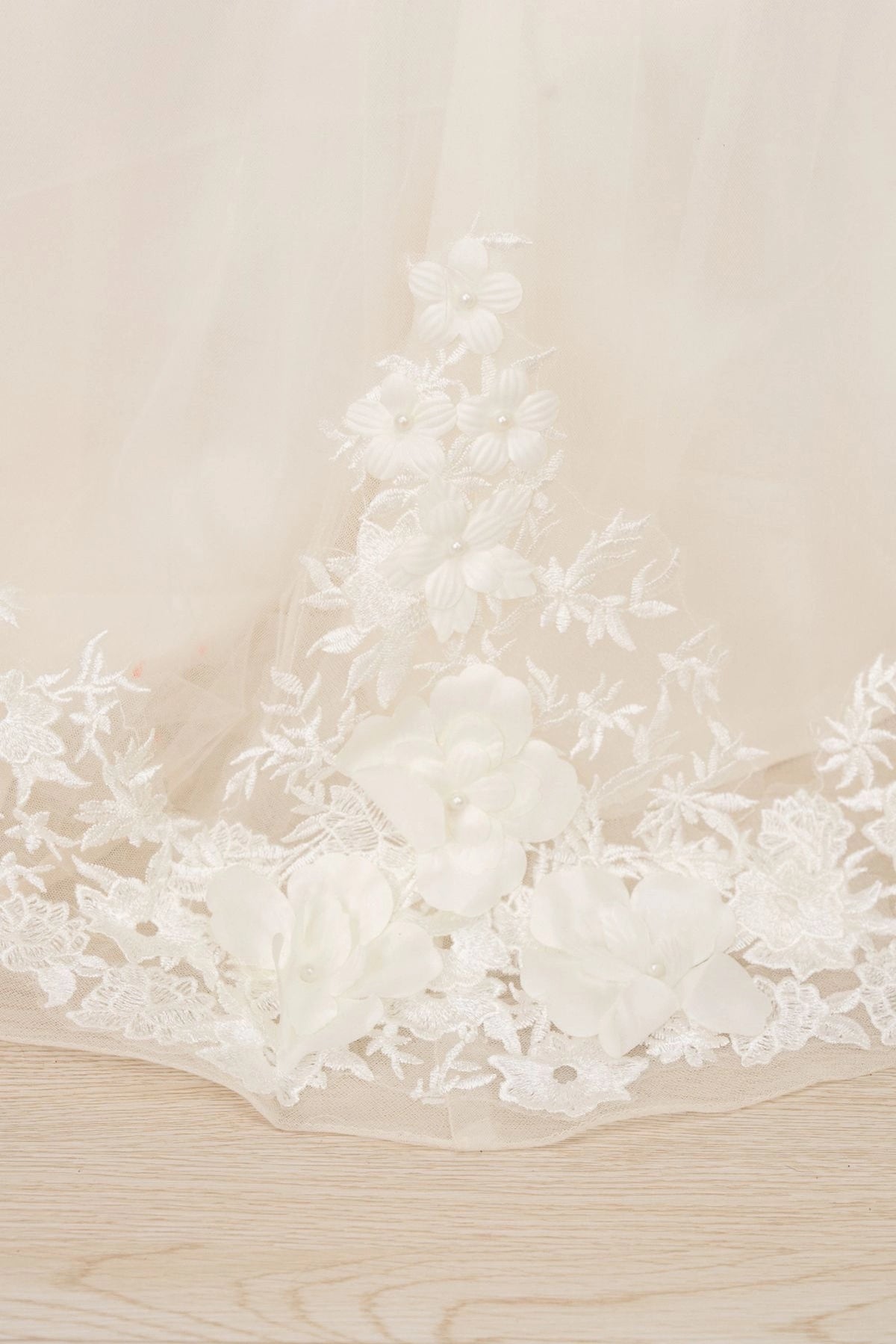 Details of the Ivory flower girl dress include raised flowers decorating the lace hem.