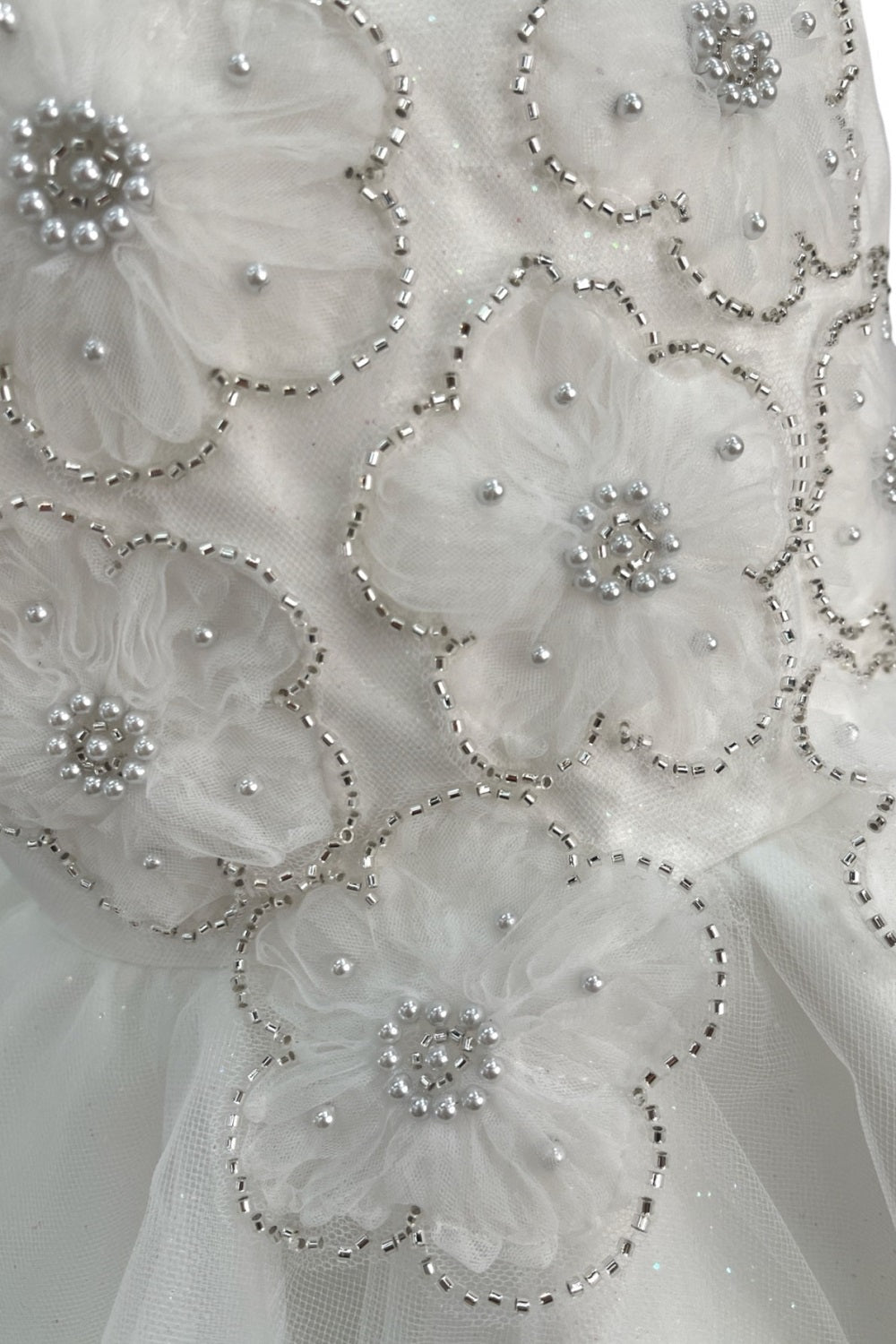 Close-up front view of ivory flower girl dress showing shimmering fabric and bow accent.