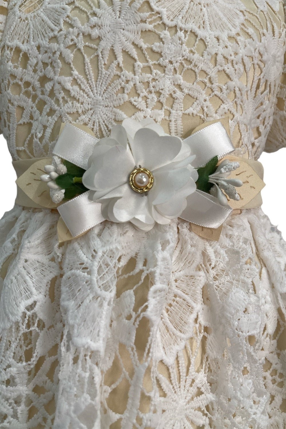 Close-up front view of champagne flower girl dress showing shimmering fabric and bow accent.