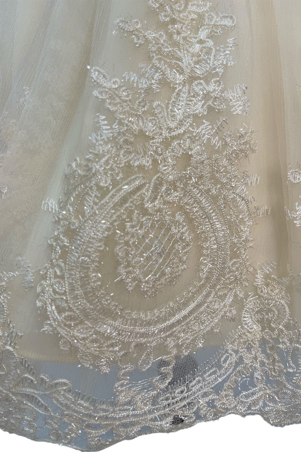 Close-up front view of cream dress showing shimmering fabric and bow accent