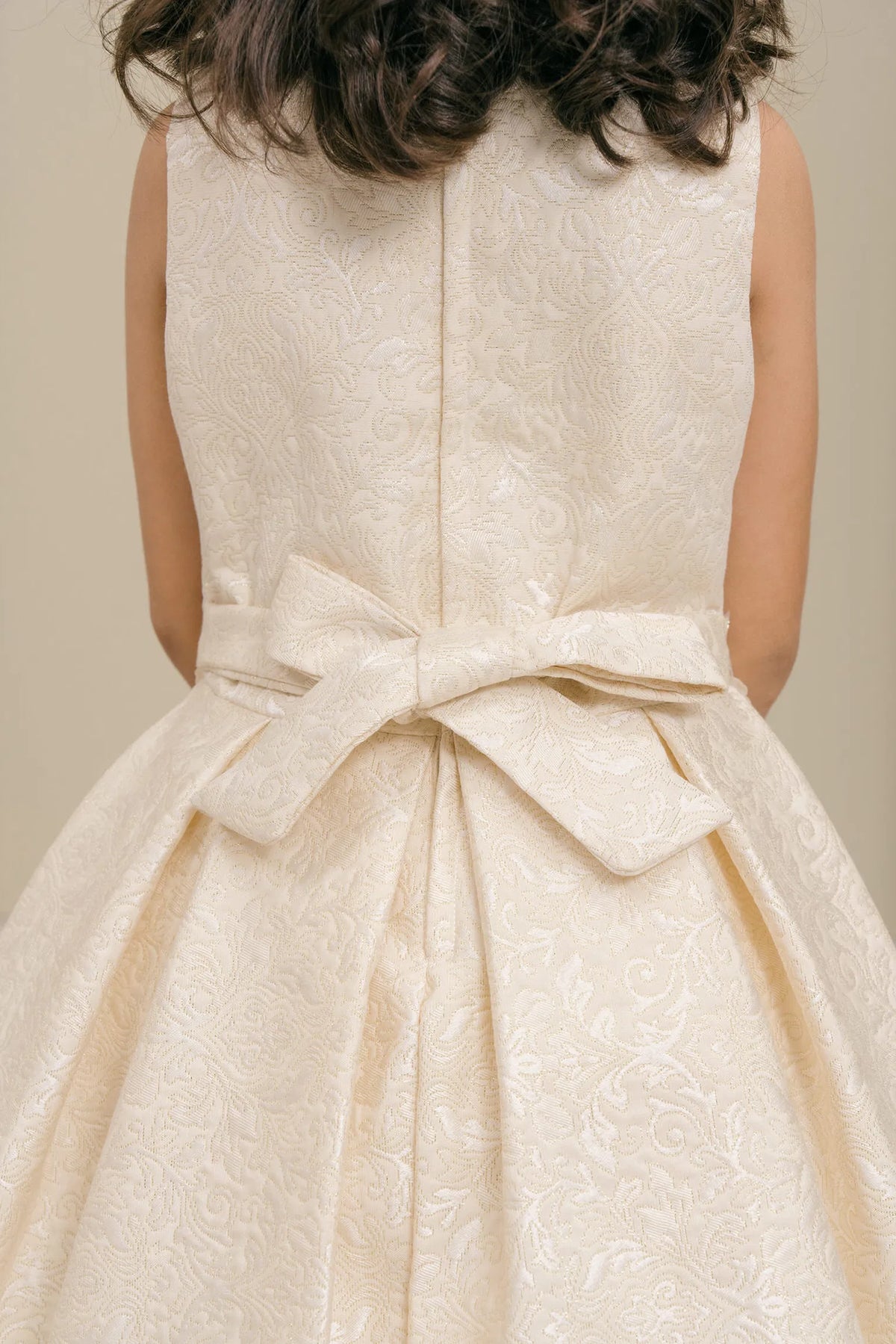 Detailed by a large waist bow, the Ivory kids party dress reveals its construction.