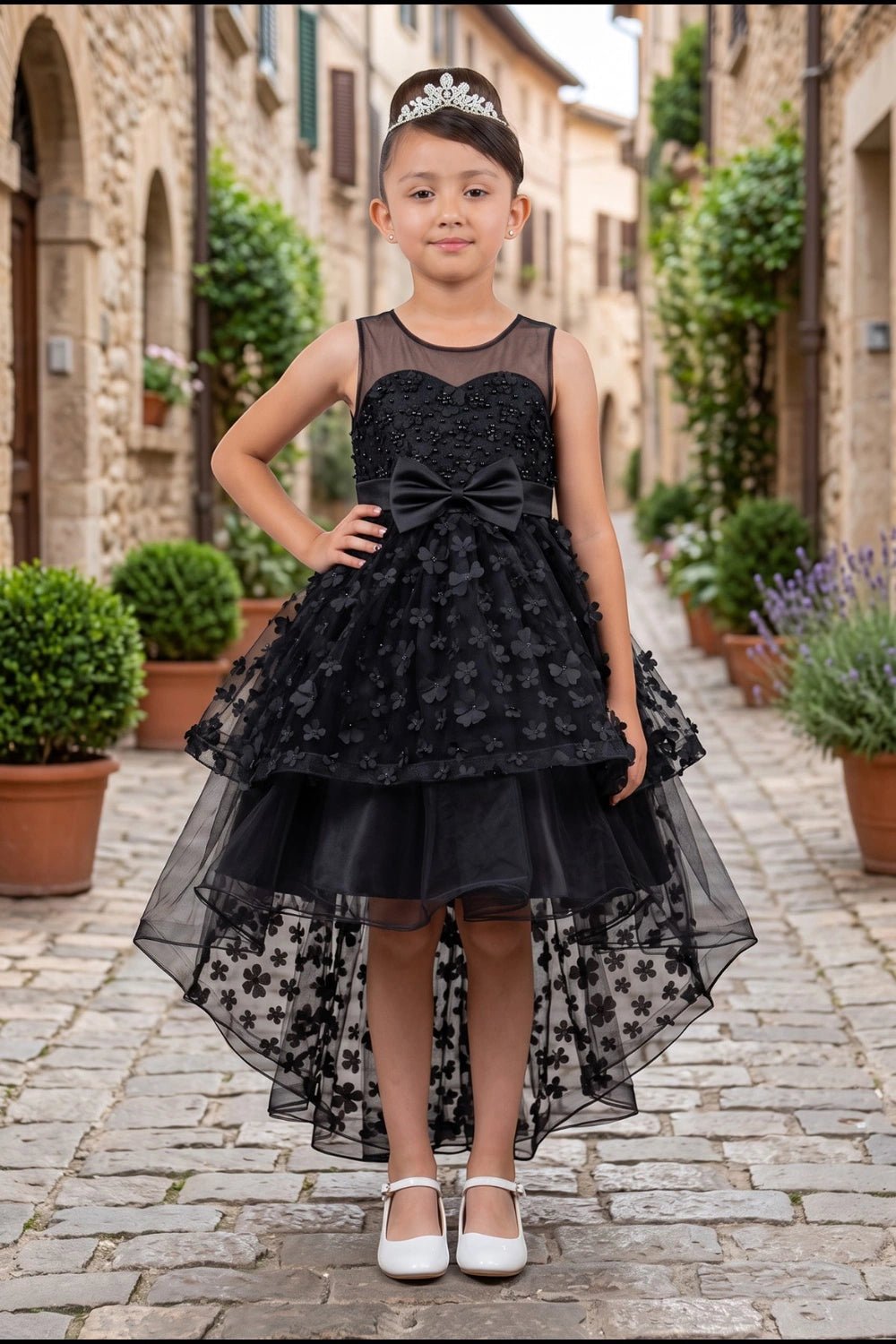 Shown in a front view, the Black flower girl dress has sheer neckline, floral overlay and bow above the high-low skirt.