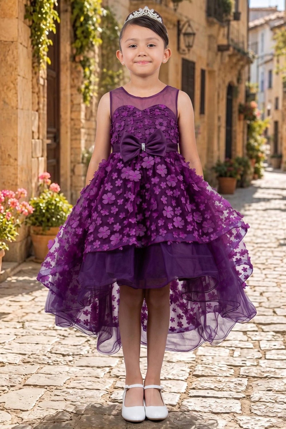 Shown in a front view, the Purple flower girl dress has sheer neckline, waist bow and layered floral high-low skirt.