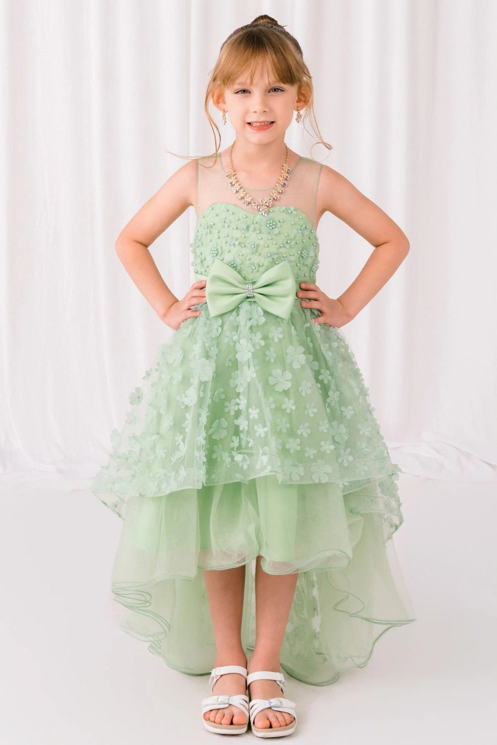 Shown in a front view, the Green (Sage) flower girl dress has floral bodice, waist bow and layered high-low tulle skirt.