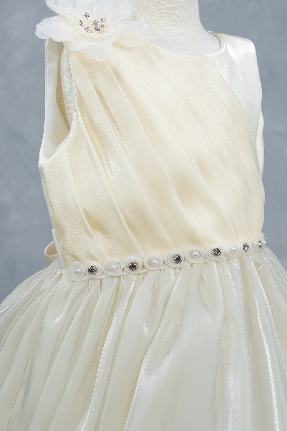 Close-up front view of ivory flower girl dress showing beadwork floral applique and pearl waist.