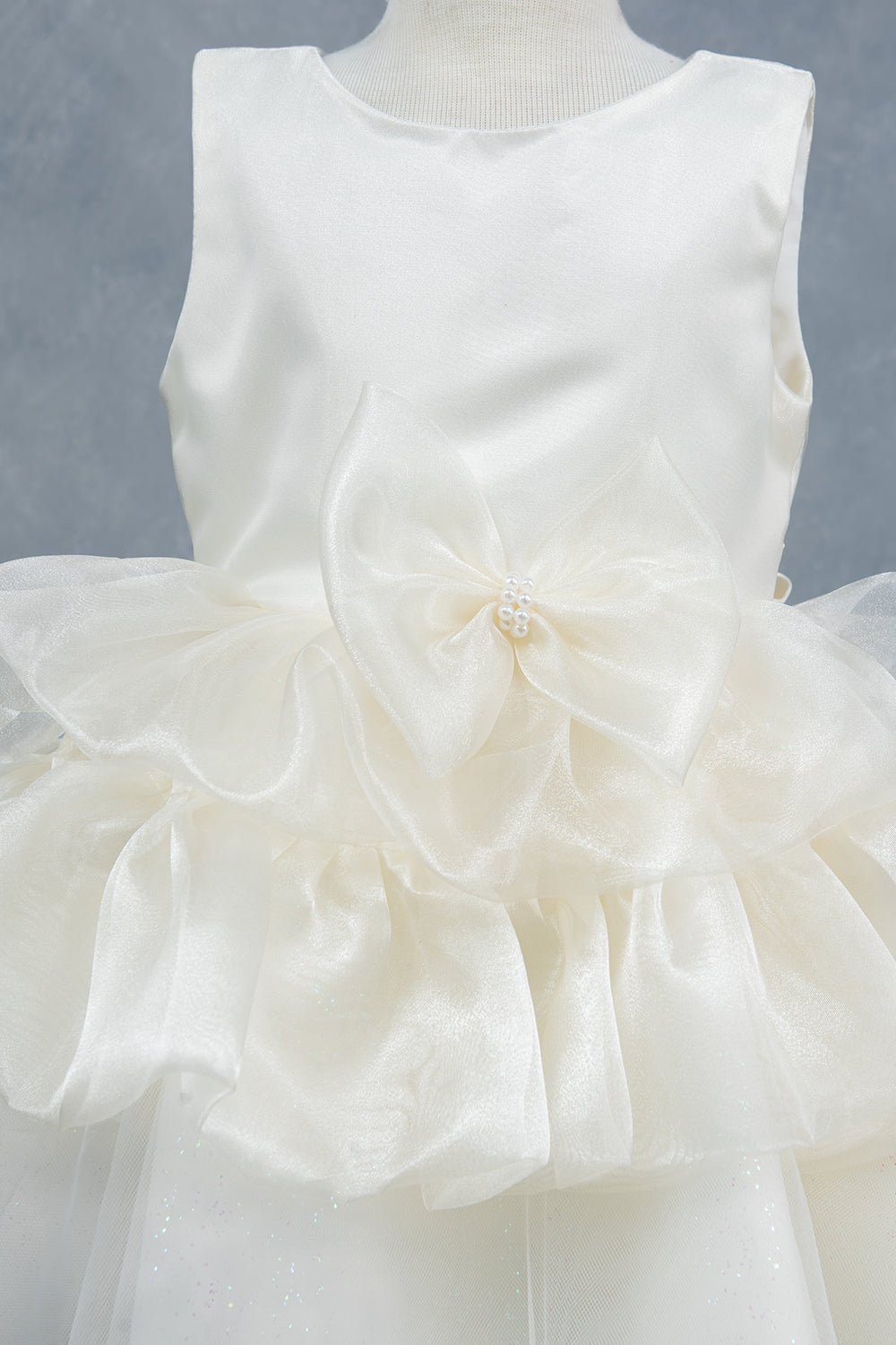Close-up front view of white flower girl dress showing floral embellishment and satin waistband.