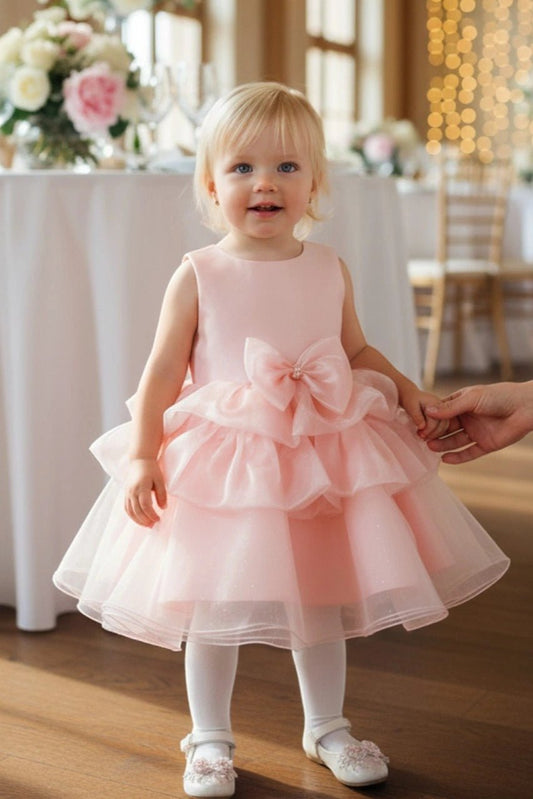 Shown in a front view, the Peach flower girl dress has sleeveless bodice and tiered tulle skirt with a waist bow.