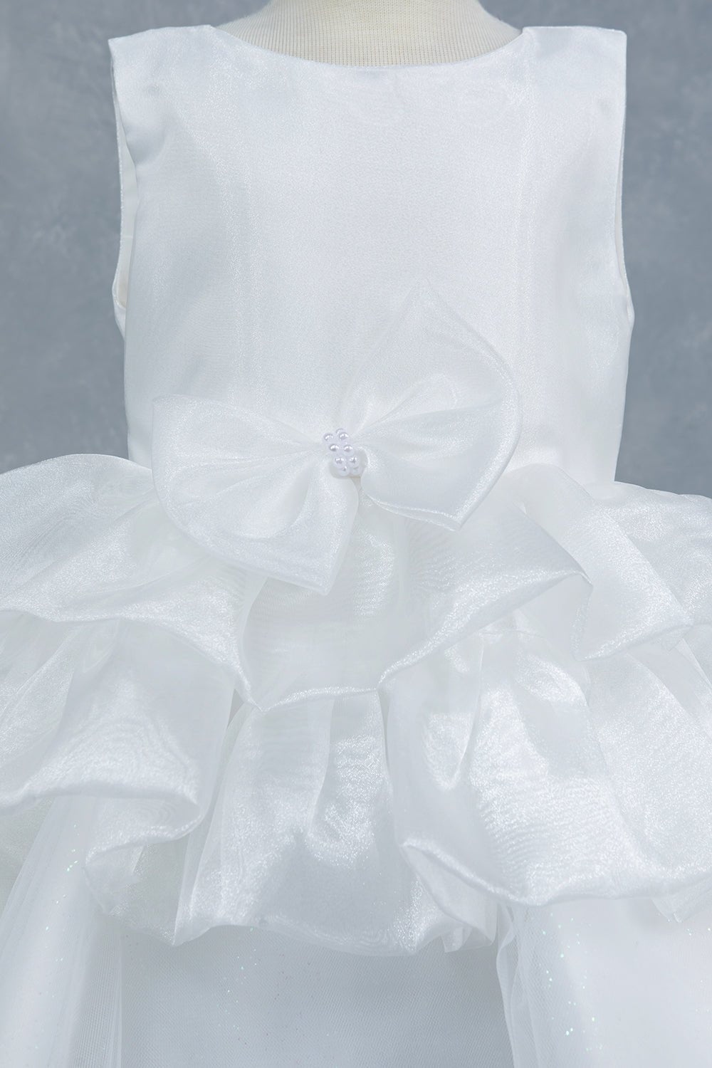 Close-up front view of white flower girl dress showing floral embellishment and satin waistband.
