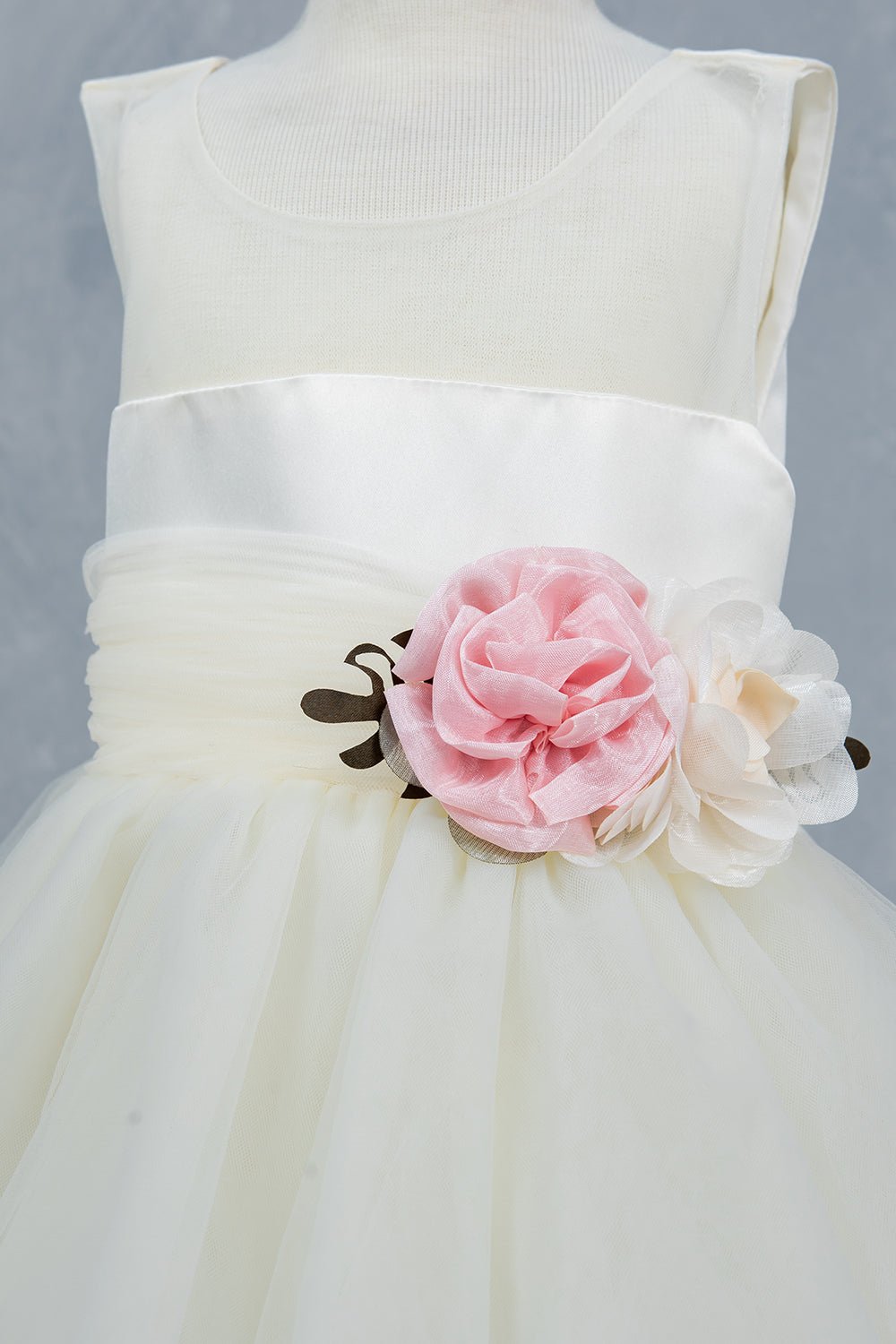 Close-up front view of ivory flower girl dress showing floral embellishment and satin waistband.